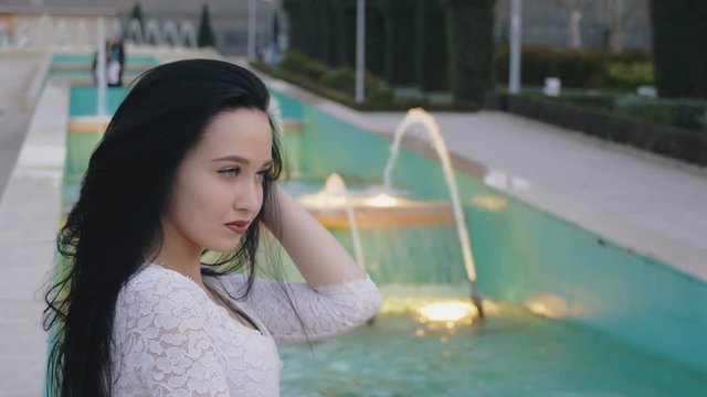 Girl flipping hair. Beautiful young woman on illuminated fountain background.