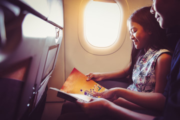 Mother with daughter sit on their place in airplane economy class and read a magazine