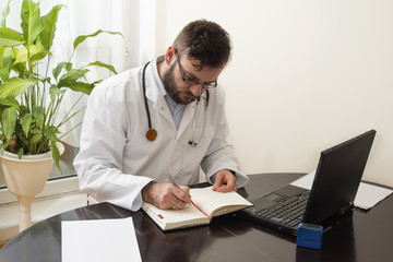 Lekarz podczas pracy. Lekarz w białym kitlu wpisuje coś do kalendarza długopisem.