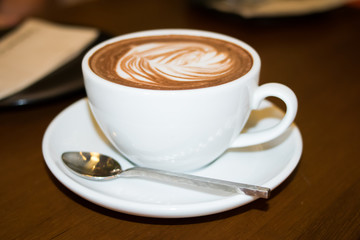 cup of coffee with heart pattern in a white cup on wooden background