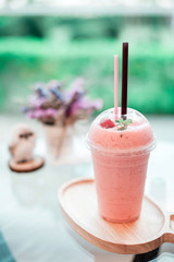 A plastic-grass of strawberry smoothie with strawberry on the top.