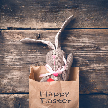 Easter bunny in a paper bag on old boards. Rabbit. Old board background. Easter ideas. Easter eggs. Space for text. Image in trendy toning. On the package text Happy Easter