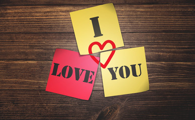 sticky notes saying I love you and red heart shape on rustic timber plank dark brown wood background