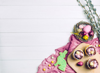 Painted eggs in natural nest, cupcakes and ginger bread on light wooden background