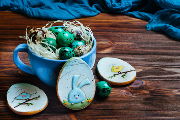 Painted quail eggs in a cup and Easter egg-shape gingerbreads on wooden table