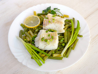 Cod fillet steamed with green beans. Concept of healthy food. Closeup on a light wooden background.