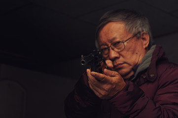 Dangerous old man pointing a gun at the target on dark background, selective focus on gun, dark tone,Crime concept