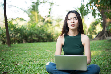 Young beautiful woman sitting on green grass and using laptop in the park with  nature background.