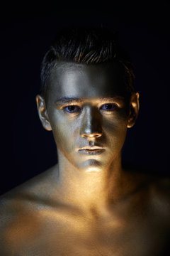 A handsome man of athletic build, completely covered in gold paint.Studio photos, With Hard lite