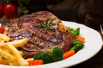 Grilled beef steak served with French fries and vegetables on a white plate.