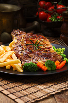 Grilled beef steak served with French fries and vegetables on a black plate.