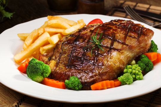Grilled beef steak served with French fries and vegetables on a white plate.