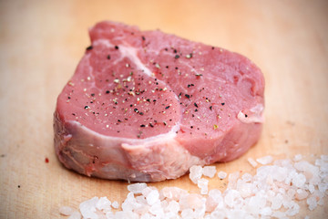 One piece of raw beef meat on wooden cutting board with pepper and  pink Himalayan salt 