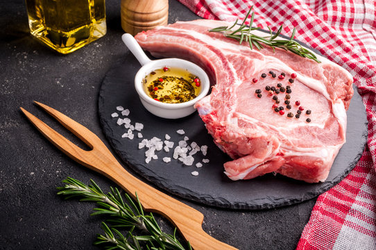 Raw meat with herbs, oil and spices on dark background. Raw pork steak. Ingredients for cooking meat