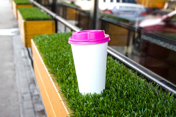 Mock up paper cup of coffee for branding .Cup of coffee with pink cap on grass . Good morning concept. Empty space for inscription.