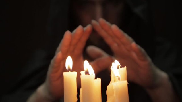 man doing the magic ritual. close-up several candle and old book. necromancer casts spells from thick ancient book by candlelight