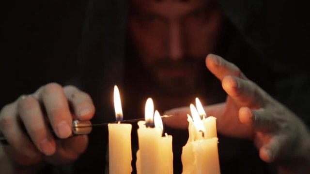 man doing the magic ritual. close-up several candle and old book. necromancer casts spells from thick ancient book by candlelight