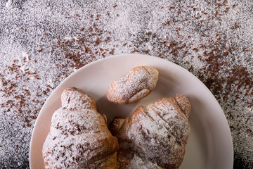 Croissants with powdered sugar and chocolate on white plate on black background. Top view. Copy space