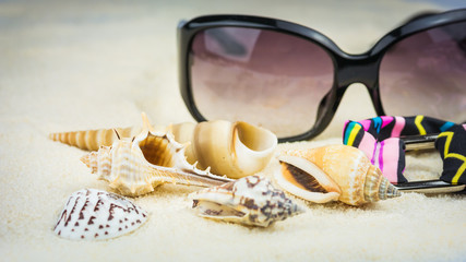 Summer holiday theme with sea shells, sunglasses and swimsuit with ethnic ornament on sandy beach