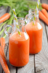 Fresh carrot juice in a bottles on rustic wooden background, selective focus