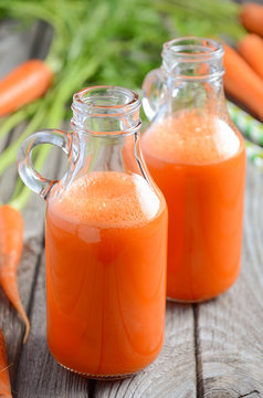Fresh carrot juice in a bottles on rustic wooden background, selective focus