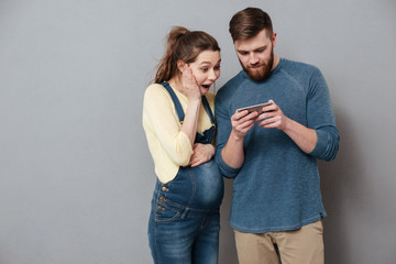 Young exciting couple looking together at mobile phone isolated