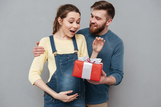 Happy cheerful husband giving present box to his pregnant wife
