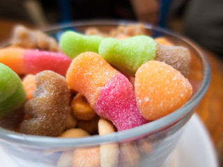 a lot of colorful candies assortment with shapes and sugar in a glass bowl. Orange, red, brown and green

