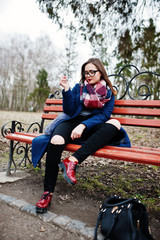 Young girl smoking cigarette outdoors sitting on bench. Concept of nicotine addiction by teenagers.