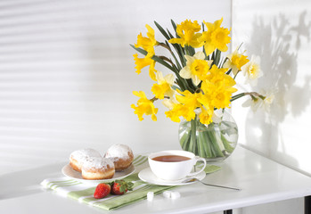 Still life with flowers daffodils white and yellow table towel green buns breakfast tea berry strawberry morning color from the window freshness