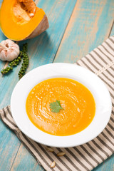  Top view of pumpkin and carrot soup with cream and parsley on blue  wooden background.