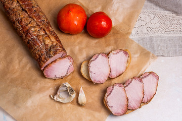 Slices smoked meat or ham on brown packing paper. Tomatoes, garlic and small snacks of bread and meat..
