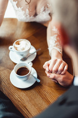 the bride and groom drinking coffee in a cafe at the round wooden table. gently holding each other's hands