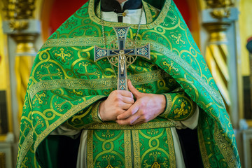 A priest in green vestments holds a large cross at his chest