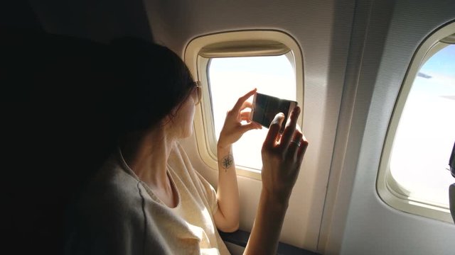 Young woman in plane taking photo on her smartphone during flight