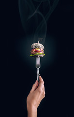 A small black hot burger is pinned on the fork. The concept of proper nutrition