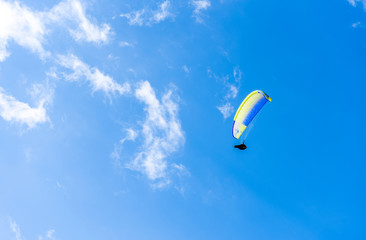 Paraglider flying against the blue sky with white clouds.