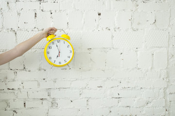 Girl holding alarm clock in her hand isolated on white brick backgroung