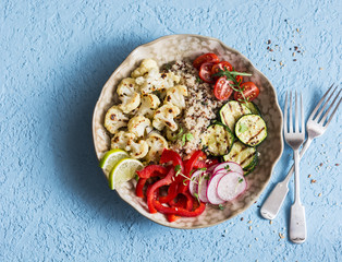 Roasted cauliflower and quinoa buddha bowl. Quinoa with cauliflower, zucchini and sweet pepper. Vegetarian healthy food concept. On a blue background, top view