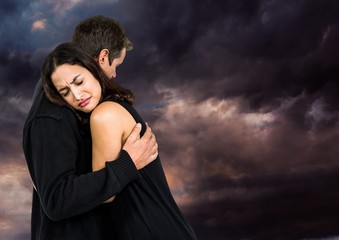 Sad couple hugging against dark cloudy sky