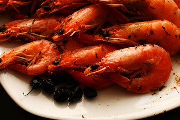 Freshly prepared shrimps lie on a white plate, adorned with spices and lemon. 