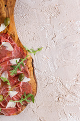 Beef carpaccio on olive wood serving board with capers, olive oil cheese and arugula, served over...