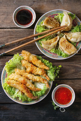 Fried tempura shrimps and gyozas potstickers on lettuce salad with sauces and rice. Served in traditional china plate with chopsticks over old wooden background. Top view. Asian dinner