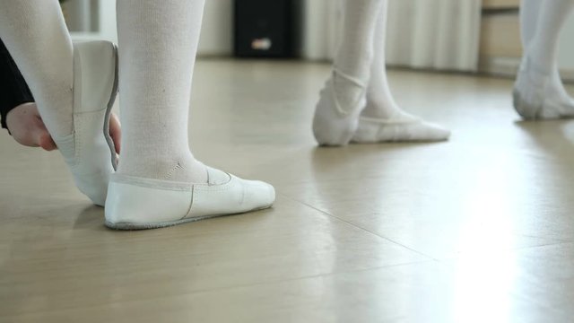 Female ballet dancer teaches and helps young dancers. Details of foot. School of ballet