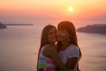 Mother and daughter at sunset. Sunset on the island of Santorini. Girl tourist on a background of the sea and the setting sun. Mother and daughter travel, Mother's love, Girl teenager and her mom.

