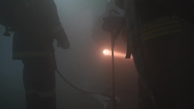 Firefighters with hoses and with flashlight in dark room