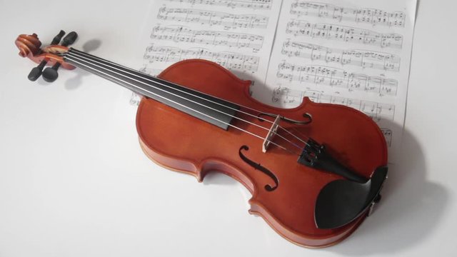 Brown violin with musical notes on a white background (spinning and panning footage). Presentation concept.