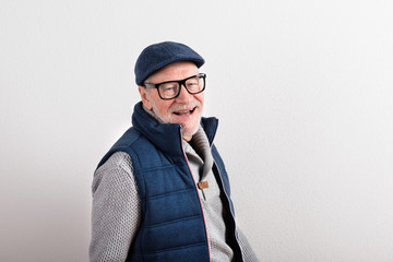 Senior man in sweater, vest jacket and cap, studio shot.