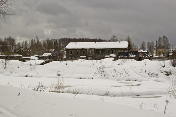 Village with old wooden houses on the banks of the river, winter, spring thaw, overcast, Russia