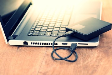 Technology concept : External hard disk and laptop computer with warm light effect.
External hard drive connected to laptop on wooden table with copy space.